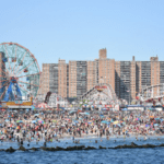 A crowded beach with ferris wheel and buildings in the background.