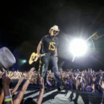 A man in a cowboy hat is standing on a stage in front of a crowd.