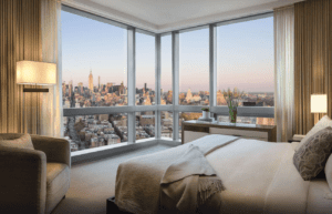 A bedroom with large windows overlooking the city.